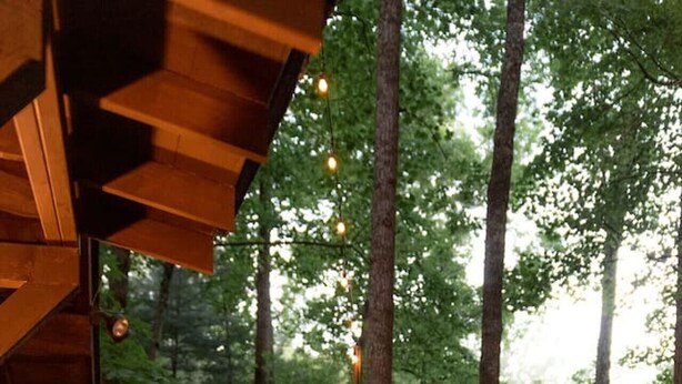 Eine Holzdielen-Terrasse mit Tisch und Stühlen, umgeben von einem Geländer und Lichterketten.