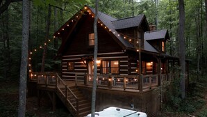 Ein rustikales Blockhaus mit Whirlpool, einer Holzterrasse und Lichterketten.