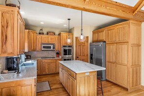 A kitchen with wooden cabinets, stainless steel appliances, a marble countertop, and a hanging pendant light.
