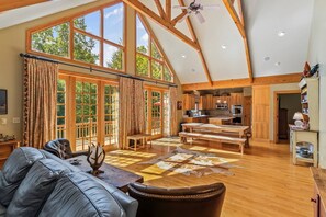 A spacious living area with a high ceiling, large windows, a wooden dining table, and a leather sofa.