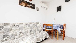 Une pièce comprenant un canapé, une table à manger avec des chaises, un climatiseur, une horloge et une petite fenêtre.