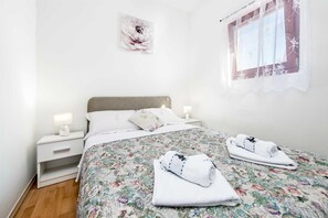 A neatly made bed with floral bedding, two bedside lamps, a nightstand, and a window with lace curtains.