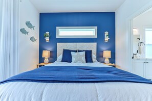 Une chambre à coucher avec un grand lit, deux tables de chevet avec des lampes, un luminaire fixé au mur et des œuvres d’art décoratives accrochées au mur.