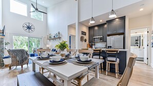 Une cuisine moderne avec des meubles de couleur sombre, des appareils en acier inoxydable et un coin repas comprenant une table et des chaises blanches.