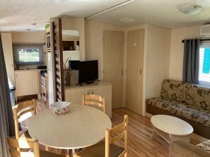 A compact living space with a dining table, chairs, a sofa, a television, and a kitchenette.