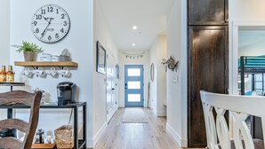 Un pasillo con un reloj, una estación de café y una puerta que da a otra habitación.