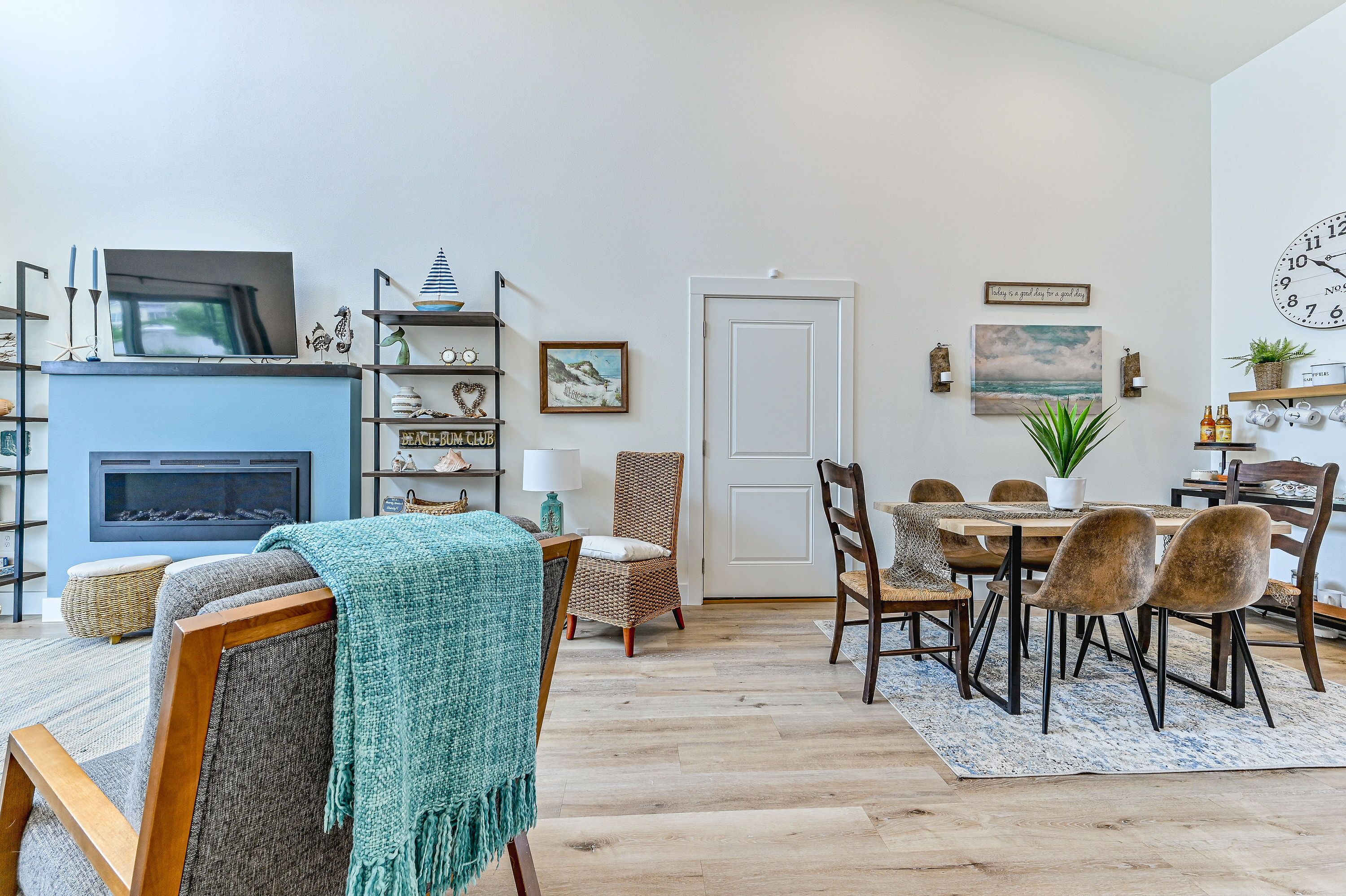 A living room with a fireplace, a dining area with a table and chairs, and a kitchen area with a clock on the wall.