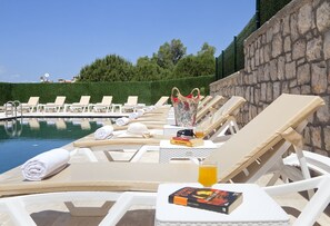 Zona de piscina con sillas de descanso, toallas y un libro.