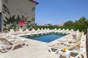 A poolside area with lounge chairs and a mural of tropical plants and flowers. - İndag Apart Aile Oteli  (Seferihisar)