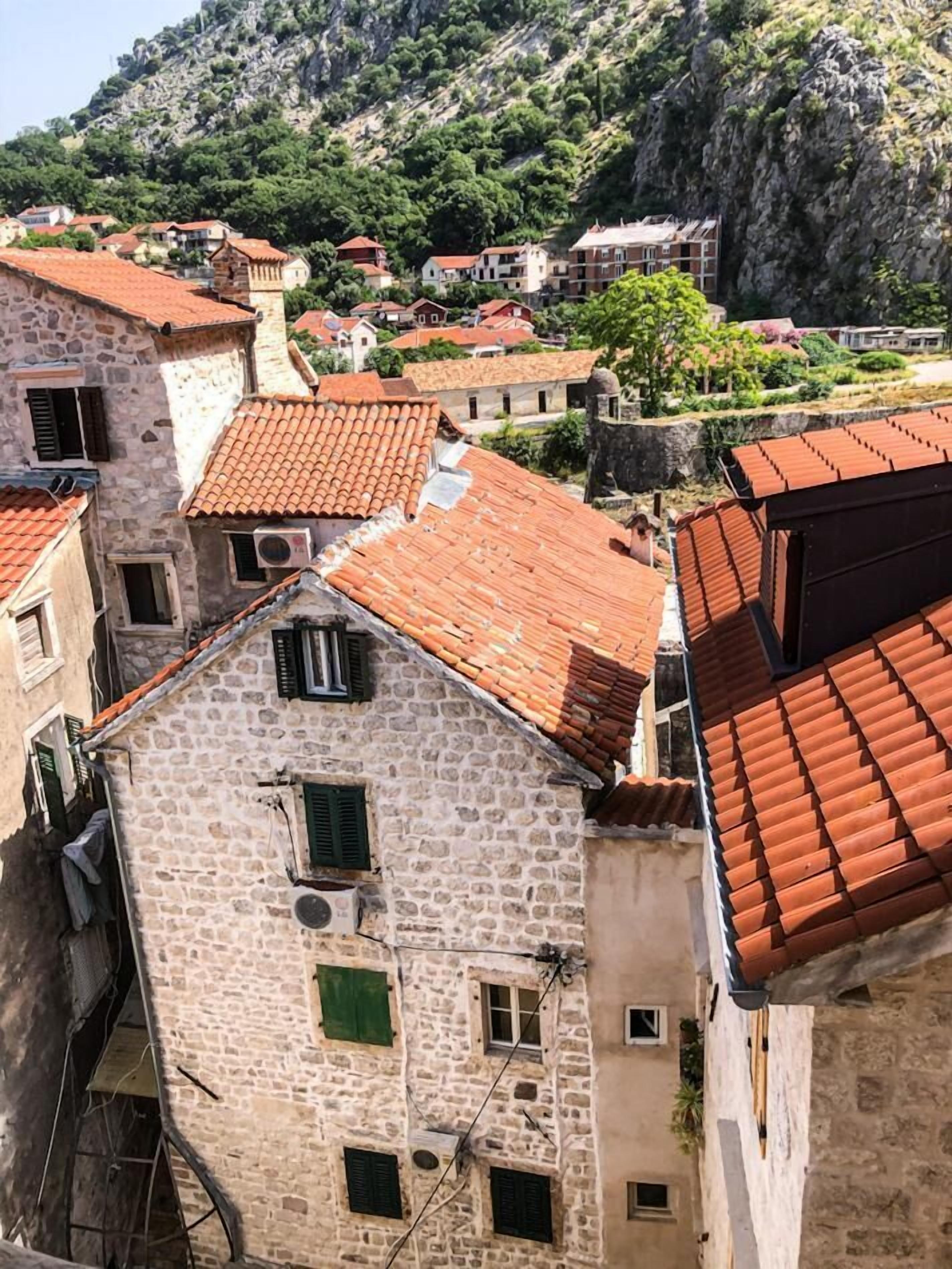 Un edificio de piedra con techo de tejas rojas, varias ventanas y vistas a una colina con otros edificios.