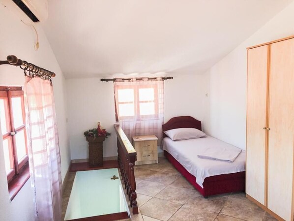 A bedroom with a single bed, a bedside table, a small cabinet, a window with curtains, and a wardrobe.