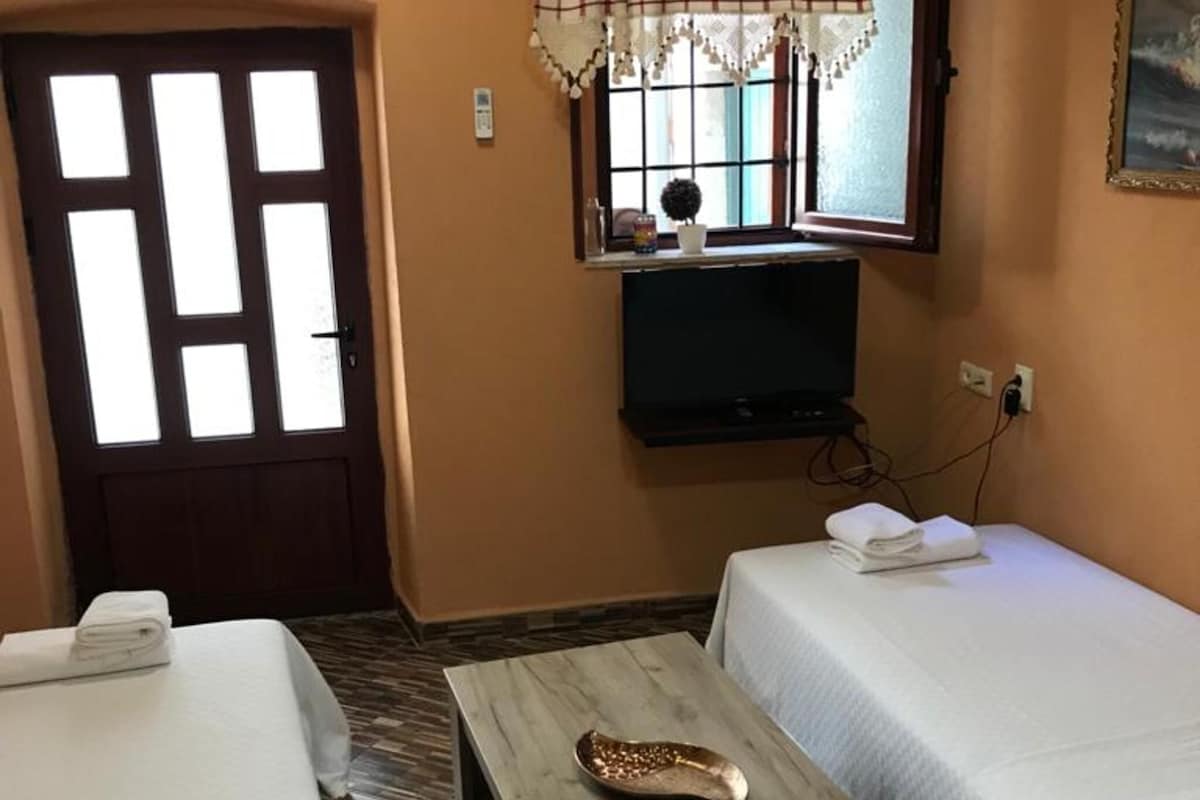 A hotel room with a bed, a bedside table, a TV, and a window with a curtain.
