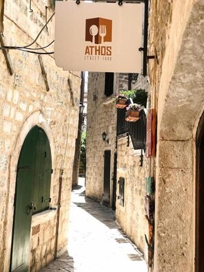A narrow street with stone buildings, a hanging sign for 'ATHOS Street Food', and a green door on the left. - Puerta Apartments (Kotor)