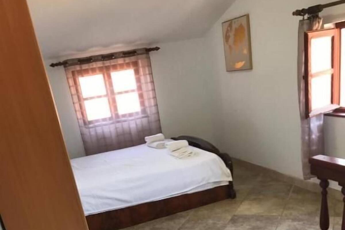 A hotel room with a bed, a small table, and a window with curtains.