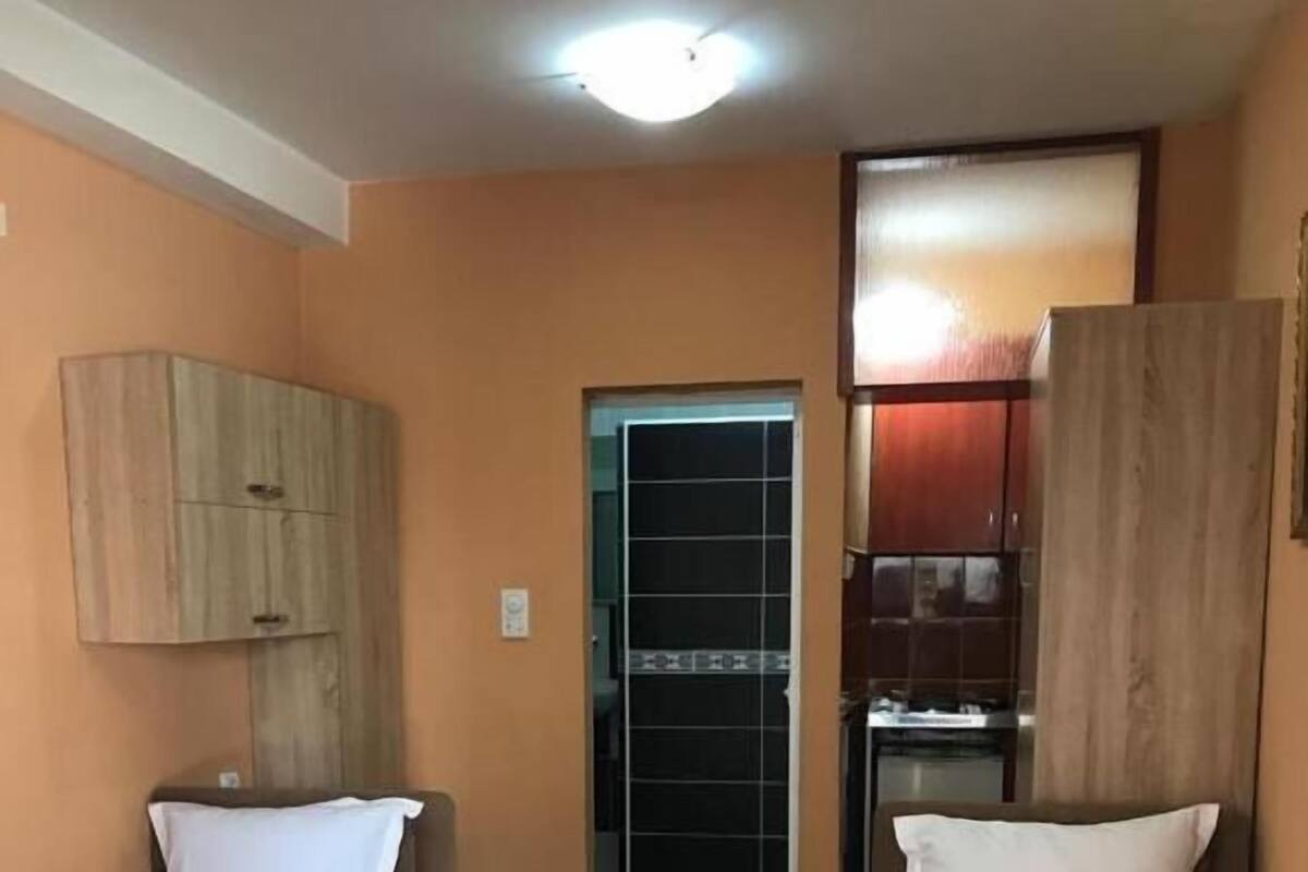 A hotel room with two single beds, a wooden table, a wardrobe, and a kitchenette.
