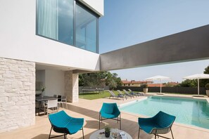 Uma área de piscina moderna ao ar livre, com muro de pedra, duas cadeiras azuis, uma mesa e um conjunto de jantar.