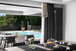 Uma área moderna para refeições ao ar livre com piscina, cadeiras preto e branco, mesa posta com flores e um grande cachepot.