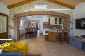 Une cuisine avec une arche en briques, des meubles en bois, un coin repas et un téléviseur.