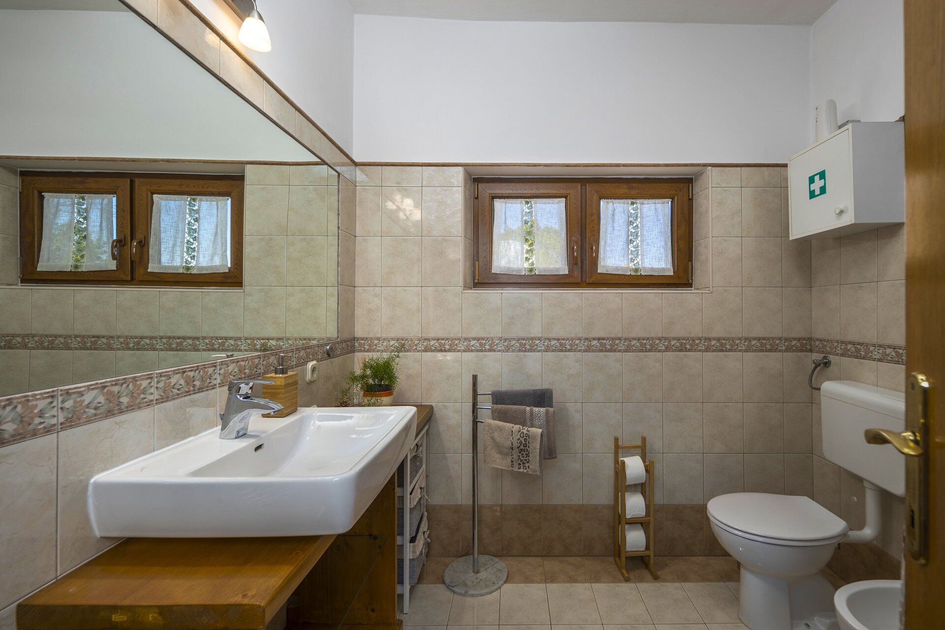 A bathroom with a sink, mirror, toilet, and a window with curtains.