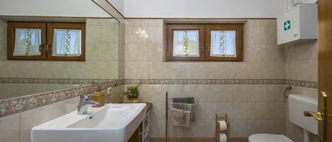 A bathroom with a sink, mirror, toilet, and a window with curtains.