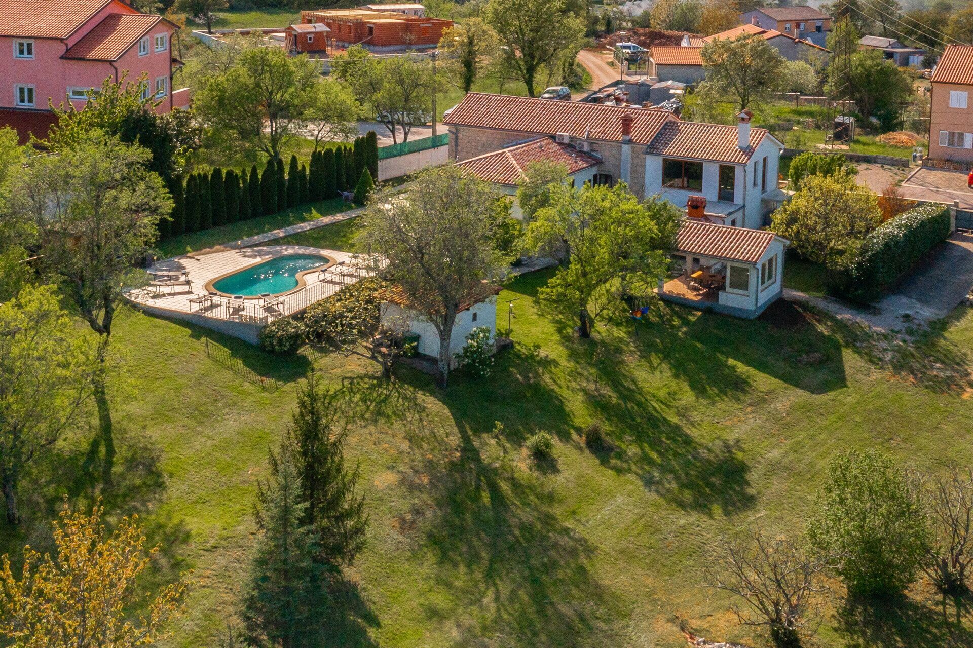 Vue aérienne d’un quartier résidentiel avec une grande maison dotée d’une piscine, entourée d’arbres et d’autres maisons.