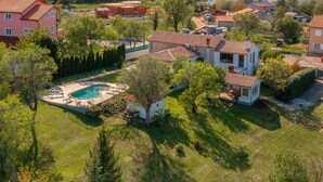 An aerial view of a residential area with a large house featuring a swimming pool, surrounded by trees and other houses. - Holiday Home Flores with Pool (Labin)