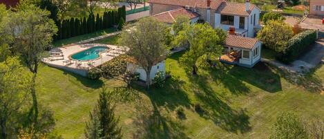 Vue aérienne d’un quartier résidentiel avec une grande maison dotée d’une piscine, entourée d’arbres et d’autres maisons.