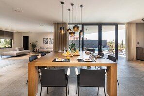 Un espace repas moderne avec une table en bois, des chaises noires et une vue sur une piscine et un coin salon extérieur.