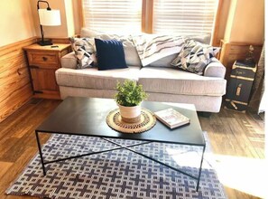 Relax in this inviting living room with a comfortable sofa, side table, and coffee table, surrounded by a potted plant and natural light.