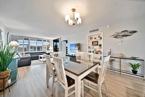 A modern living room with a dining area, large windows, and a view of the sea.