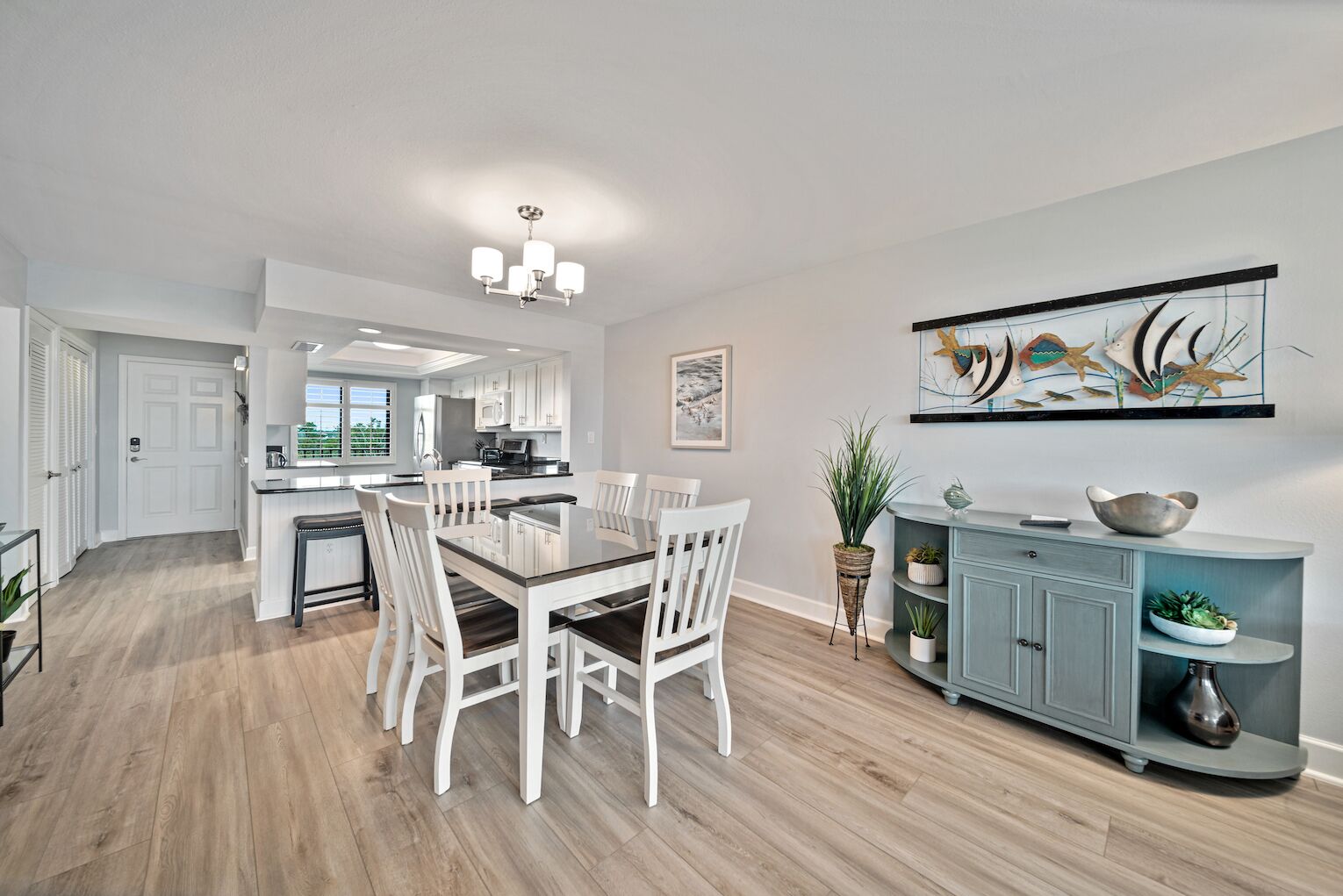 A modern kitchen with white cabinetry, a dining area with a glass-top table and white chairs, and a blue console with decorative items.