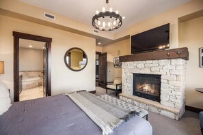 A bedroom with a stone fireplace, a large bed, a round mirror, and a television mounted on the wall.