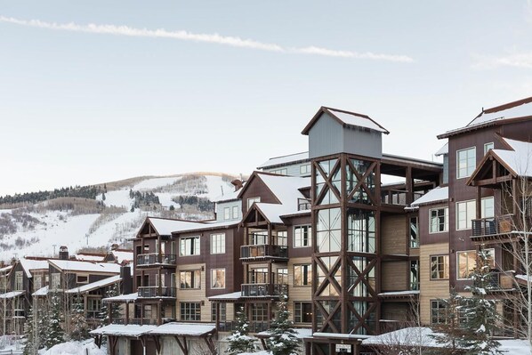 A multi-story hotel with a wooden exterior and large windows, set in a snowy mountainous area. - Silver Star 4302 | Apres Ski Hot Tub (Park City)