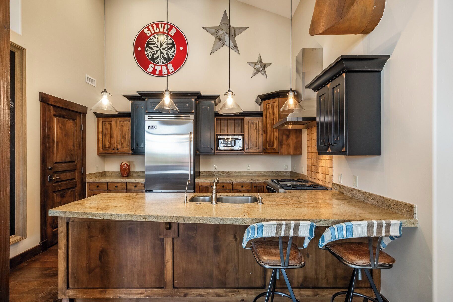 Una cocina con una isla central, armarios de madera, un refrigerador de acero inoxidable e iluminación colgante.