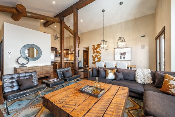 A spacious living room with a large wooden coffee table, leather sofas, and a dining area with a white table and chairs.