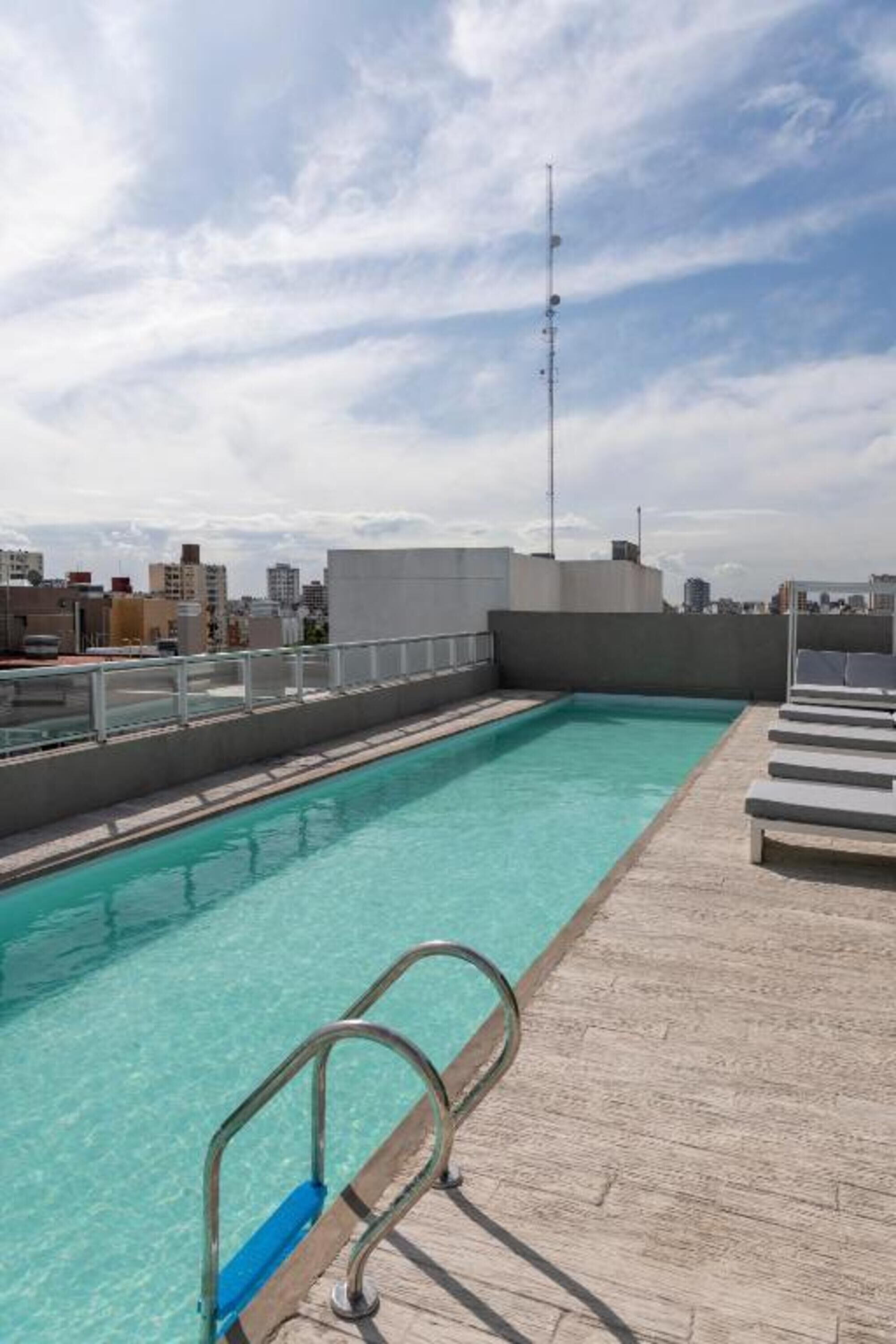 A rooftop swimming pool with clear blue water, a metal ladder, and lounge chairs.