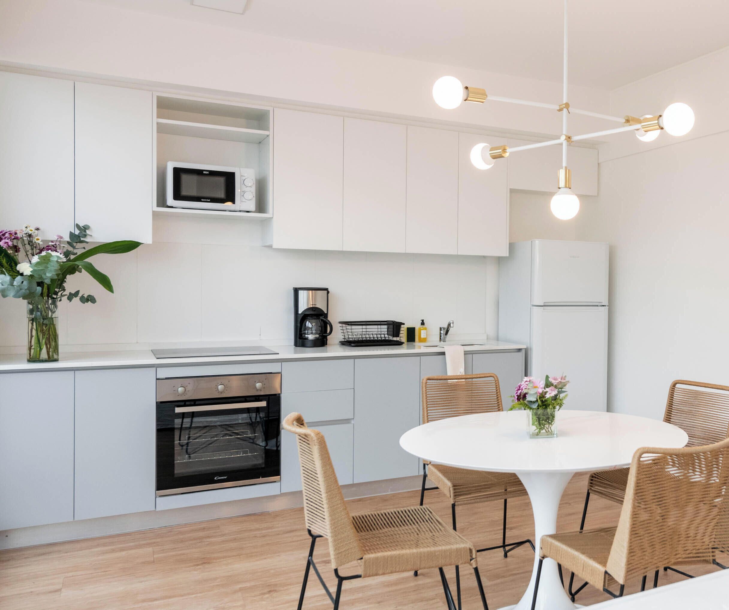 A modern kitchen with white cabinetry, a built-in microwave, a coffee maker, and a dining area with wicker chairs and a white table.