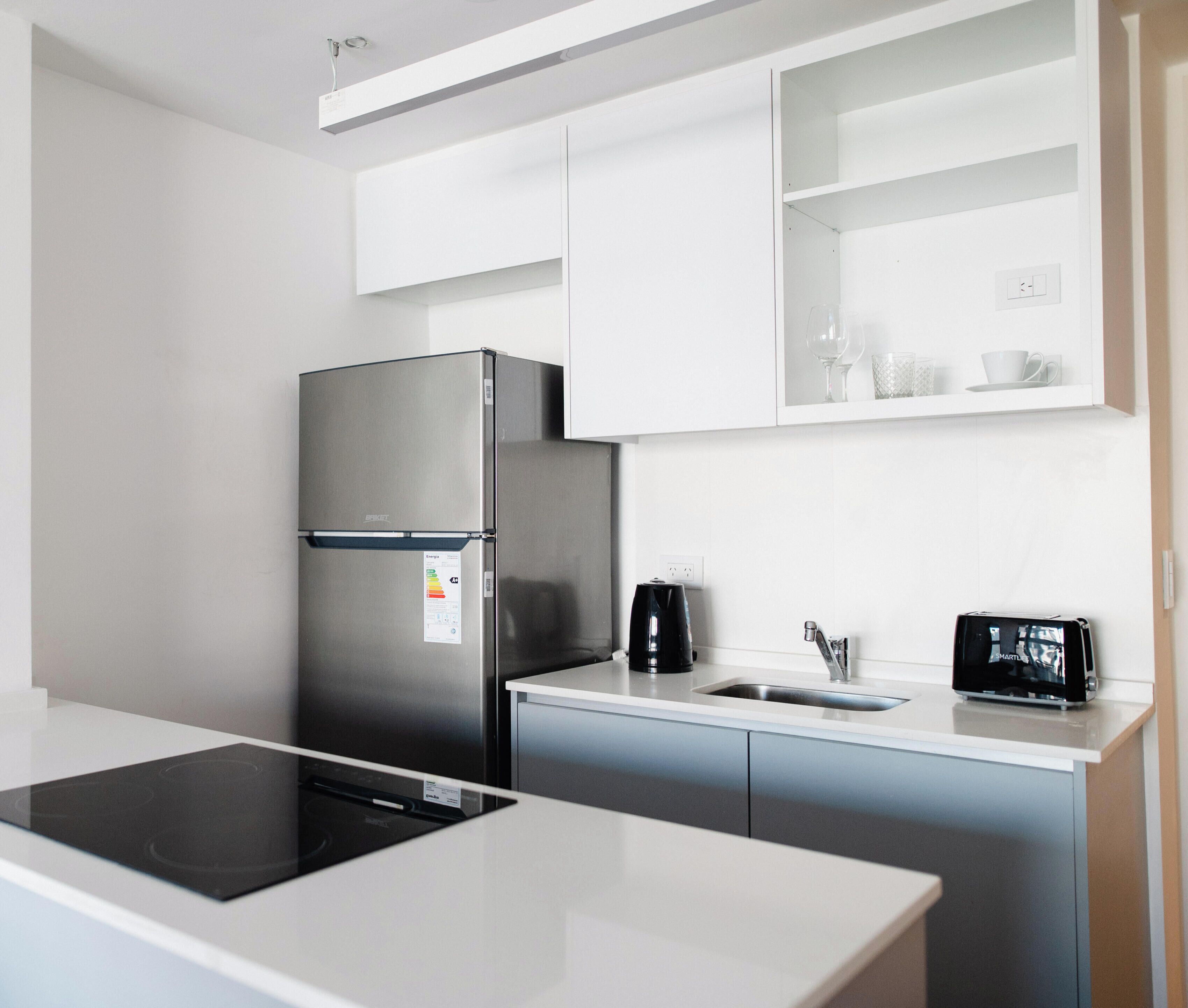 A modern kitchen with a stainless steel refrigerator, a built-in stove, a coffee maker, and a sink.