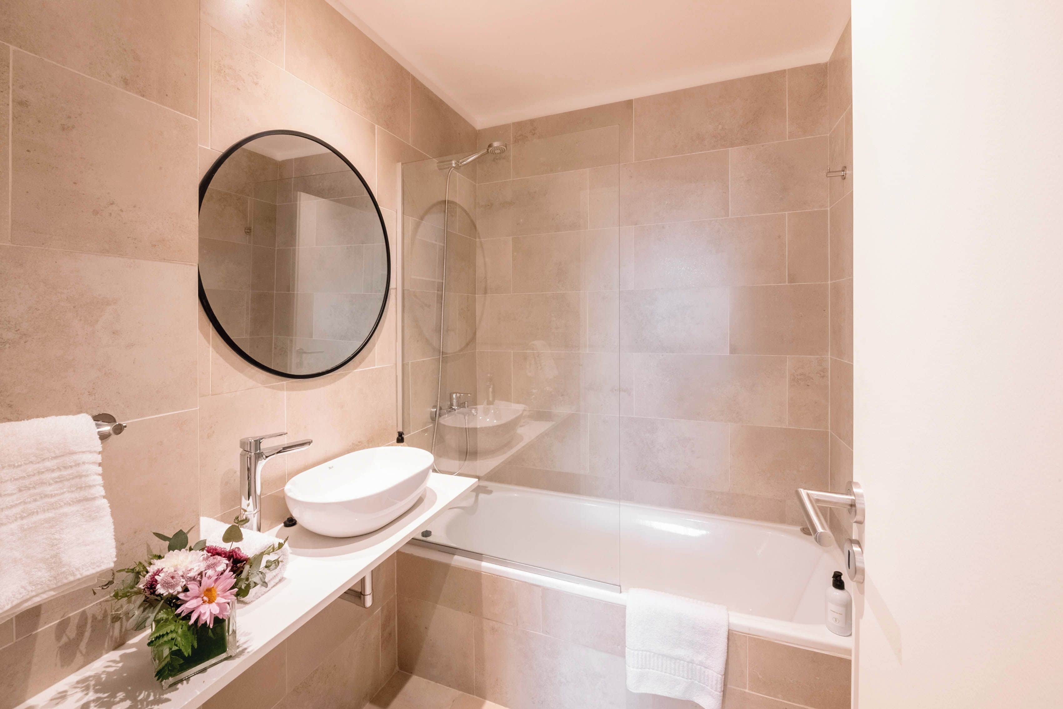 A modern bathroom with a round mirror, a white sink, a bathtub, and a shower.