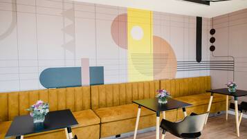 Un interior moderno con un sofá amarillo, mesas negras y un mural geométrico en la pared.
