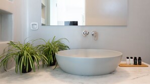 Een moderne badkamer met een groot wit wastafelmeubel, twee potplanten, een spiegel en een klein houten plankje met drie flessen.