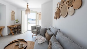 Een moderne woonkamer met een grijze bank, houten bijzettafels, een eethoek met een houten tafel en stoelen, en een wand versierd met wandkunst van geweven materiaal.