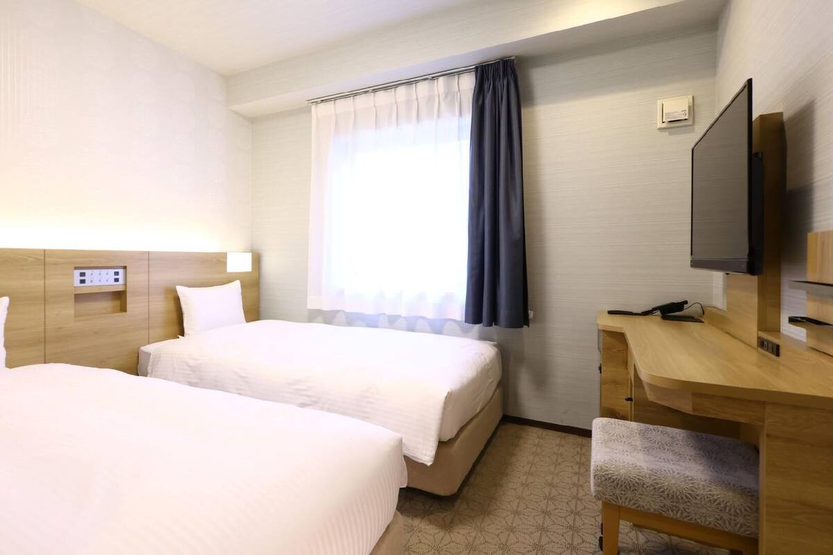 Habitación de hotel con dos camas, un escritorio, un televisor y una ventana con cortinas.