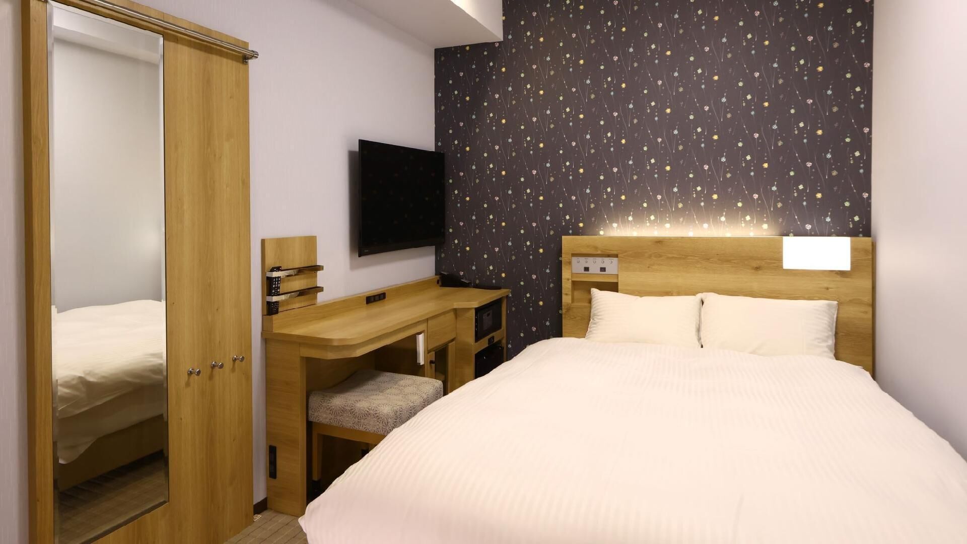 A bedroom with a bed, a desk, a chair, a wardrobe, and a TV.