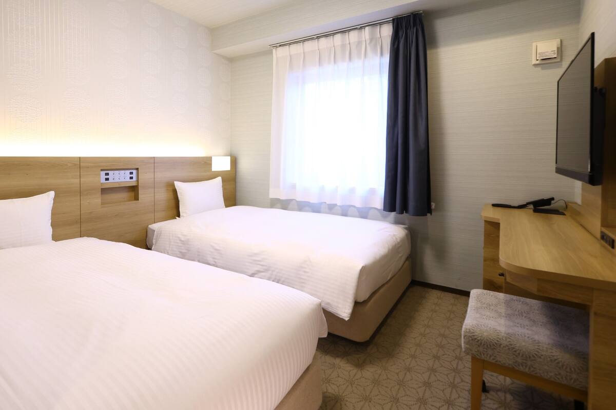 Habitación de hotel con dos camas, un escritorio, un televisor y una ventana con cortinas.