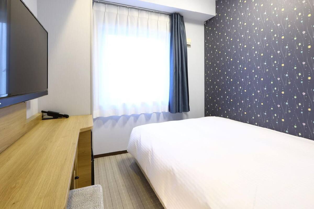 Una habitación de hotel con cama, televisor, escritorio y ventana con cortinas.