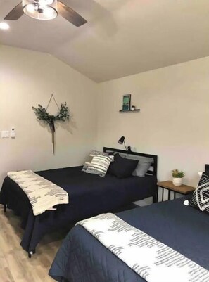Two single beds with dark-colored bedspreads and a throw blanket, set against a simple, clean backdrop.