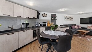 A modern kitchen with a dining area, a living room with a sofa and TV, and a clock on the wall.