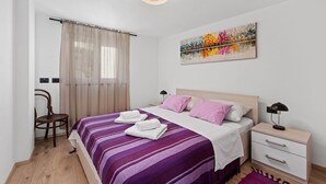 A bedroom with a bed, a chair, a nightstand, and a painting on the wall.