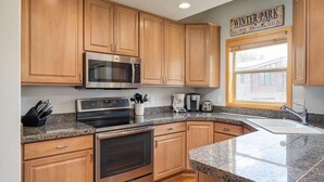 A kitchen with wooden cabinets, a stainless steel microwave, a built-in oven, granite countertops, and a window with a sign reading 'Winter Park.'